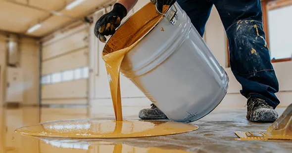 Craftsman pouring epoxy material onto floor for durable finish in Denver, Colorado.